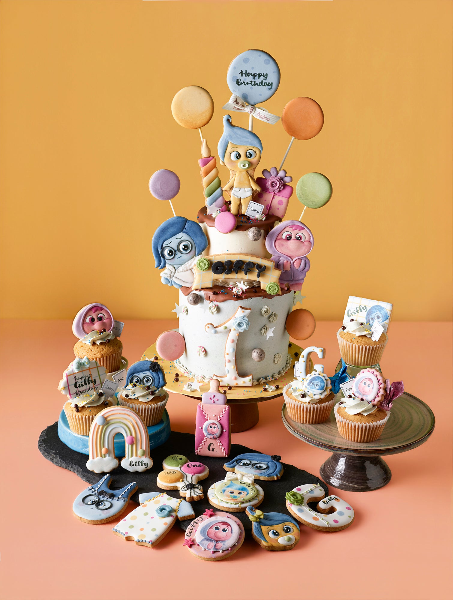 Amico Pasticceria 訂製《玩轉腦朋友》(Inside Out) 嬰兒主題大型派對套餐，專為一歲生日設計。包含一個以 BB 版阿愁 (Sadness)、阿樂 (Joy) 等角色及氣球裝飾的雙層專屬生日蛋糕，並搭配同主題的精緻杯子蛋糕，以及彩虹、奶瓶、嬰兒包屁衣造型的手工糖霜曲奇。